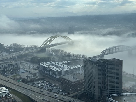 Aerial view of golden arches piercing through a sea of swirling mist casting a muted glow over the dark urban landscape Cincinnati Ohio United States.