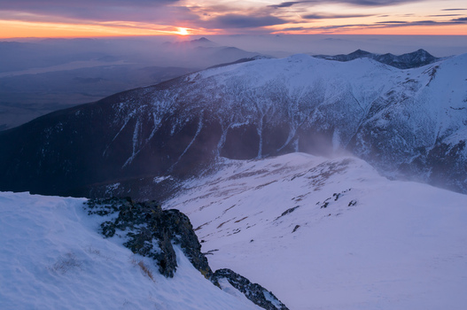 View of the snowy peak of Baranec in the Western Tatras during a sunset with strong winds blowing snow across the ridge in Jamnik Zilina Region Slovakia. View of the snowy peak of Baranec in the Western Tatras during a sunset with strong winds blowing snow across the ridge in Jamnik Zilina Region Slovakia.