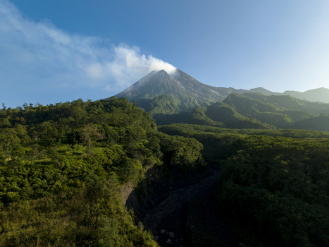 Aerial view of Mount Merapi with smoke rising from the crater above lush green tropical forests and a deep valley Kecamatan Pakem Daerah Istimewa Yogya Indonesia. Aerial view of Mount Merapi with smoke rising from the crater above lush green tropical forests and a deep valley Kecamatan Pakem Daerah Istimewa Yogya Indonesia.
