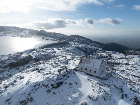 Aerial view of a snow laden landscape featuring a solitary white building against the backdrop of a serene partially frozen lake Lagoa Comprida São Romão Serra da Estrella Portugal. Aerial view of a snow laden landscape featuring a solitary white building against the backdrop of a serene partially frozen lake Lagoa Comprida São Romão Serra da Estrella Portugal.
