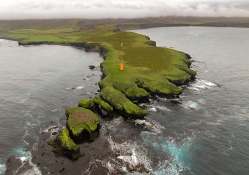 Aerial view of the Tjornes peninsula featuring dramatic coastal cliffs lush green grassy terrain and an orange radio tower surrounded by the Atlantic Ocean in Tjorneshreppur Iceland. Aerial view of the Tjornes peninsula featuring dramatic coastal cliffs lush green grassy terrain and an orange radio tower surrounded by the Atlantic Ocean in Tjorneshreppur Iceland.