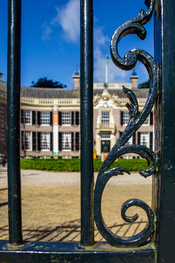 View of Castle Groeneveld seen through the ornate scrollwork of a black wrought iron gate under a clear blue sky Baarn Utrecht Netherlands.