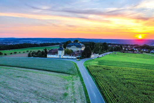 Aerial view of Schloss Jagersburg surrounded by lush green fields and a rural road under a vibrant sunset sky in Eggolsheim Bayern Germany.