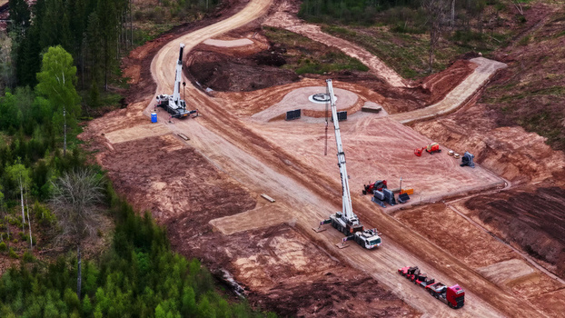 Aerial view of wind turbine base construction with cranes and heavy machinery on a cleared forest site in Latvia. Aerial view of wind turbine base construction with cranes and heavy machinery on a cleared forest site in Latvia.