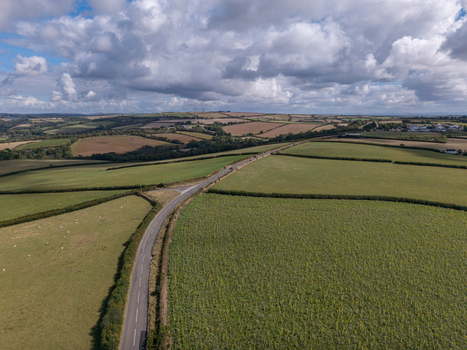 Aerial view of rural farmland featuring green fields hedgerows a winding road and freshly harvested crops under a cloudy sky in Looe Cornwall United Kingdom. Aerial view of rural farmland featuring green fields hedgerows a winding road and freshly harvested crops under a cloudy sky in Looe Cornwall United Kingdom.