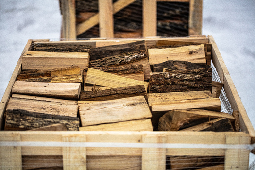 View of a wooden crate filled with neatly stacked chopped firewood pieces with snow visible in the background Latvia. View of a wooden crate filled with neatly stacked chopped firewood pieces with snow visible in the background Latvia.