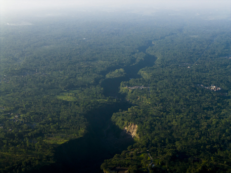 Aerial view of the deep Kali Gendol river valley surrounded by dense tropical forest and lush greenery under a hazy morning sky in Cangkringan Special Region of Yogyakarta Indonesia.