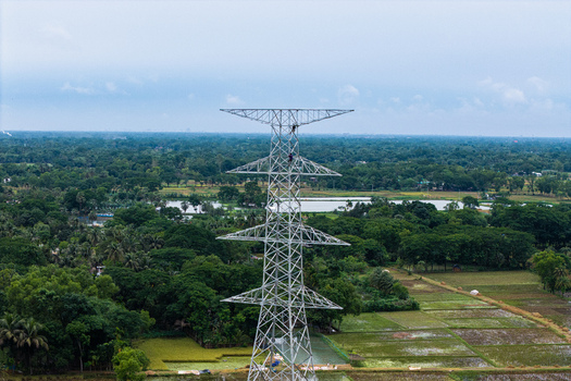 Trishal Upazila Bangladesh 13 May 2026 Aerial view of a high voltage electricity pylon with workers climbing the structure amidst lush green fields and rural landscapes. Trishal Upazila Bangladesh 13 May 2026 Aerial view of a high voltage electricity pylon with workers climbing the structure amidst lush green fields and rural landscapes.