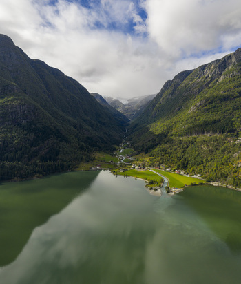 Aerial view of the turquoise Sandvinvatnet lake and lush green valley surrounded by steep mountains under a cloudy sky in Sandvin Vestland Norway. Aerial view of the turquoise Sandvinvatnet lake and lush green valley surrounded by steep mountains under a cloudy sky in Sandvin Vestland Norway.