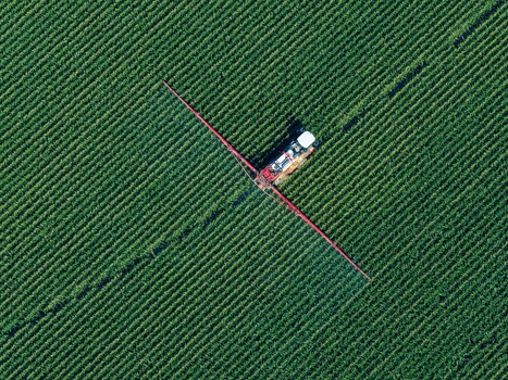 Aerial view of a tractor spraying a green agricultural field with long booms in Hombourg Grand Est France. Aerial view of a tractor spraying a green agricultural field with long booms in Hombourg Grand Est France.