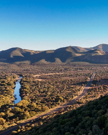 Aerial view of a long road winding through a remote mountain landscape with a river running alongside the route through dense bushveld in Thabazimbi Limpopo South Africa.