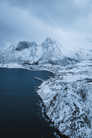 Aerial view of the village nestled between the dark sea and snow laden mountains under a brooding sky Mefjordvær Troms Norway. Aerial view of the village nestled between the dark sea and snow laden mountains under a brooding sky Mefjordvær Troms Norway.