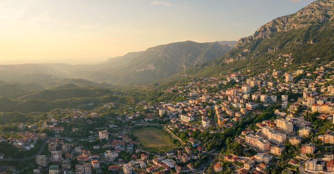 Aerial view of the historic town and a football stadium nestled at the foot of rugged mountains under a warm golden sunset light in Kruje Durres County Albania.