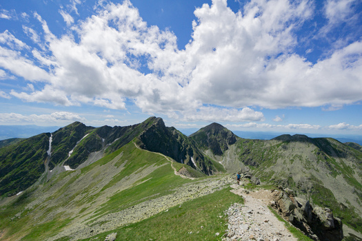 View of Tri kopy in Western Tatras with sharp rocky peaks green alpine slopes and a winding hiking trail under a blue sky with white clouds in Ziar Zilina Region Slovakia. View of Tri kopy in Western Tatras with sharp rocky peaks green alpine slopes and a winding hiking trail under a blue sky with white clouds in Ziar Zilina Region Slovakia.