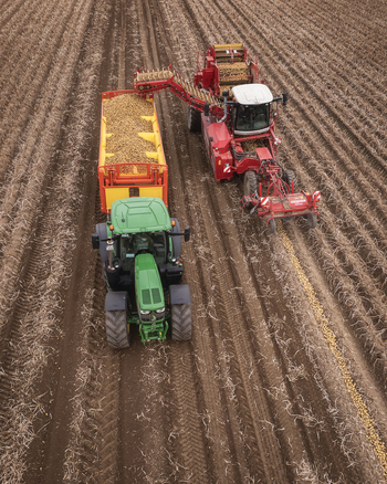 Aerial view of Keogh s Farm with a red potato harvester transferring potatoes into a yellow trailer pulled by a green tractor in a brown field Oldtown County Dublin Ireland. Aerial view of Keogh s Farm with a red potato harvester transferring potatoes into a yellow trailer pulled by a green tractor in a brown field Oldtown County Dublin Ireland.