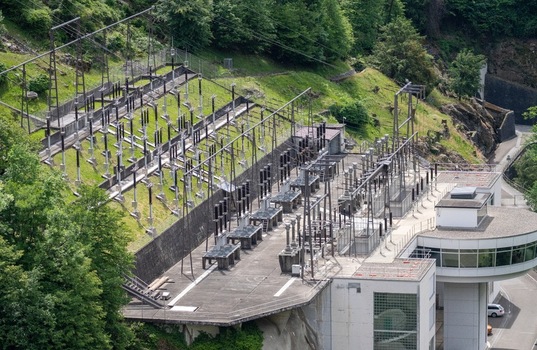 Aerial view of the electrical substation and power plant infrastructure at the Verzasca Dam with high voltage lines and lush green hillsides in Gordola Ticino Switzerland. Aerial view of the electrical substation and power plant infrastructure at the Verzasca Dam with high voltage lines and lush green hillsides in Gordola Ticino Switzerland.