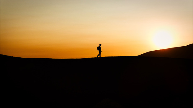Aerial view of a lone hiker silhouetted against the setting sun on the volcanic slopes of Mount Etna under a warm orange sky in Castiglione di Sicilia Sicily Italy. Aerial view of a lone hiker silhouetted against the setting sun on the volcanic slopes of Mount Etna under a warm orange sky in Castiglione di Sicilia Sicily Italy.