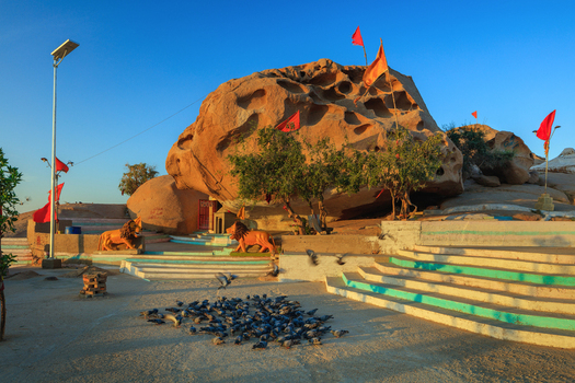 View of Chorio temple with its distinctive rock formation orange flags lion statues and pigeons on the ground in Nagarparkar Sindh Pakistan.