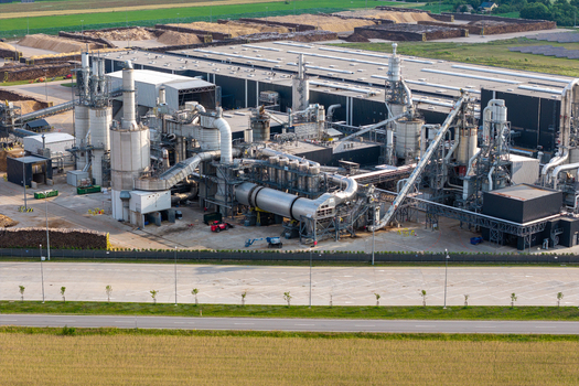 Aerial view of the wood processing installation in a large particleboard production plant with industrial silos complex piping systems and piles of wood chips in Poland.