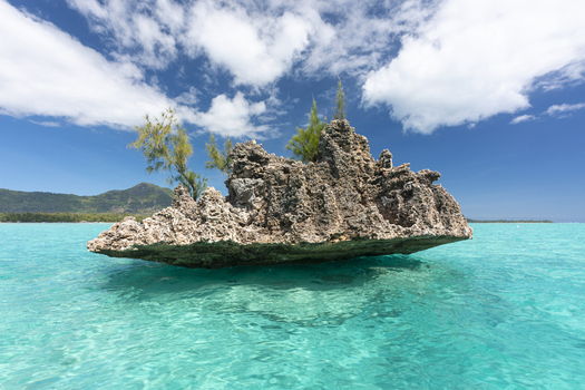 View of the Crystal Rock formation surrounded by turquoise ocean water under a blue sky with white clouds in Mauritius Mauritius.