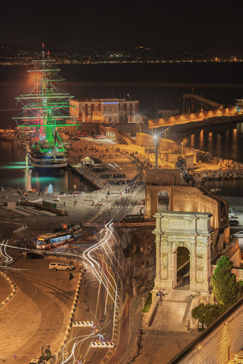 Ancona Italy 12 October 2022 View of the Arch of Trajan and the illuminated Amerigo Vespucci sailing ship docked in the port of Ancona at night.