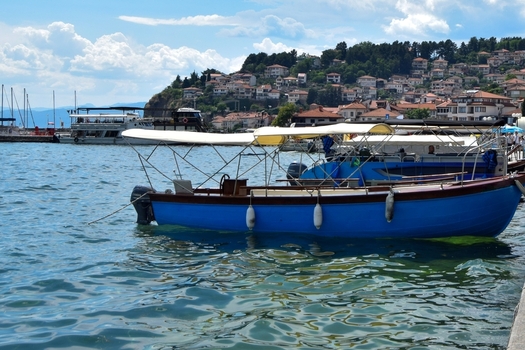 View of a blue boat with a canopy docked on Lake Ohrid with the historic town of Ohrid and its hillside houses in the background Ohrid Municipality of Ohrid North Macedonia. View of a blue boat with a canopy docked on Lake Ohrid with the historic town of Ohrid and its hillside houses in the background Ohrid Municipality of Ohrid North Macedonia.