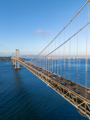 Aerial view of the San Francisco Oakland Bay Bridge with traffic flowing across the suspension structure over the blue waters of the bay in San Francisco California United States. Aerial view of the San Francisco Oakland Bay Bridge with traffic flowing across the suspension structure over the blue waters of the bay in San Francisco California United States.