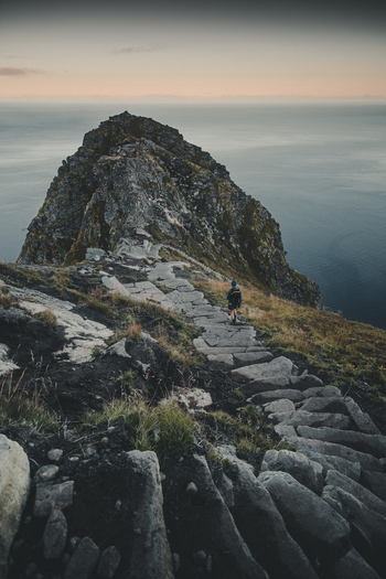 View of Reinebringen mountain trail with a hiker walking on stone steps overlooking the sea at sunset in Moskenes Nordland Norway.
