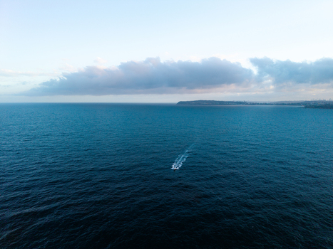 Aerial view of a small boat leaving a wake on the deep blue ocean near the coastline of Dee Why New South Wales Australia. Aerial view of a small boat leaving a wake on the deep blue ocean near the coastline of Dee Why New South Wales Australia.