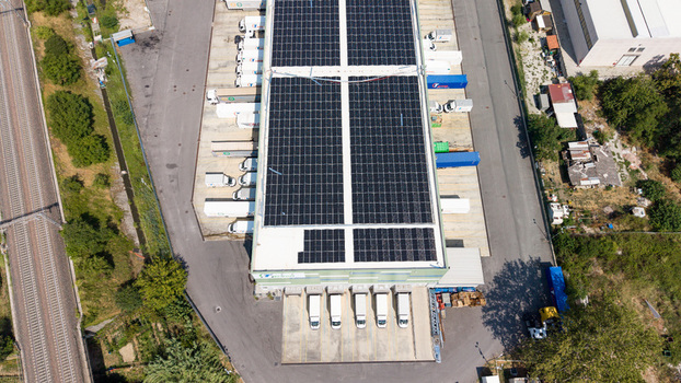 Aerial view of a logistics hub with solar panels on the roof loading docks with parked trucks and adjacent railway tracks in Melegnano Lombardy Italy.