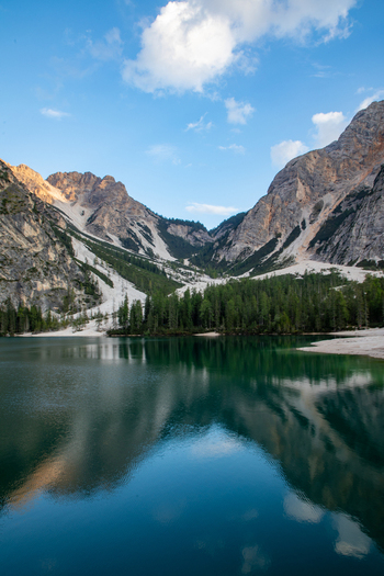 View of the Dolomites mountains reflecting in the calm turquoise waters of a mountain lake surrounded by pine forests under a clear blue sky in Rocca Pietore Veneto Italy. View of the Dolomites mountains reflecting in the calm turquoise waters of a mountain lake surrounded by pine forests under a clear blue sky in Rocca Pietore Veneto Italy.
