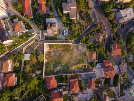Aerial view of residential houses with red tiled rooftops winding roads and a walled plot of land surrounded by lush greenery during golden hour Kruje Durres County Albania.