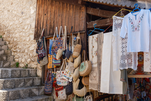 View of traditional handmade souvenirs including woven bags and embroidered shirts hanging at a shop in the historic bazaar of Kruje Durres County Albania.