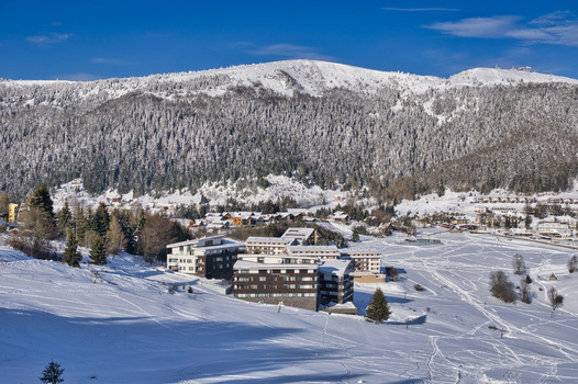 View of snow laden buildings nestled in a valley where a mountain covered in snow dusted trees rises majestically against a clear blue sky Donovaly Slovakia. View of snow laden buildings nestled in a valley where a mountain covered in snow dusted trees rises majestically against a clear blue sky Donovaly Slovakia.
