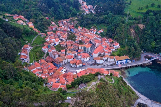 Aerial view of colorful houses built into the steep cliffs of a lush green valley overlooking the blue sea Cudillero Asturias Spain. Aerial view of colorful houses built into the steep cliffs of a lush green valley overlooking the blue sea Cudillero Asturias Spain.