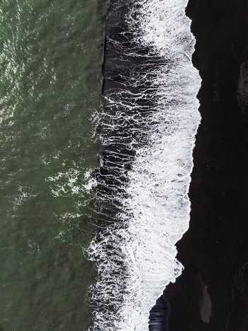 Aerial view of white sea foam crashing against the black sand beach of the Icelandic coastline in Iceland. Aerial view of white sea foam crashing against the black sand beach of the Icelandic coastline in Iceland.
