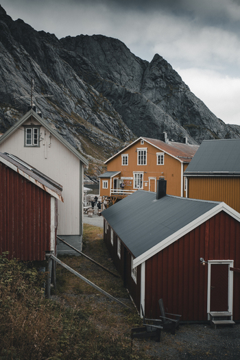 Nusfjord Nordland Norway 07 September 2022 View of the historic fishing village of Nusfjord with iconic red and yellow wooden houses nestled against dramatic mountains under a cloudy sky. Nusfjord Nordland Norway 07 September 2022 View of the historic fishing village of Nusfjord with iconic red and yellow wooden houses nestled against dramatic mountains under a cloudy sky.