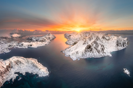 Aerial view of the snow covered peaks of the Lofoten islands during a vibrant golden sunset over the Arctic sea in Nordland Norway.