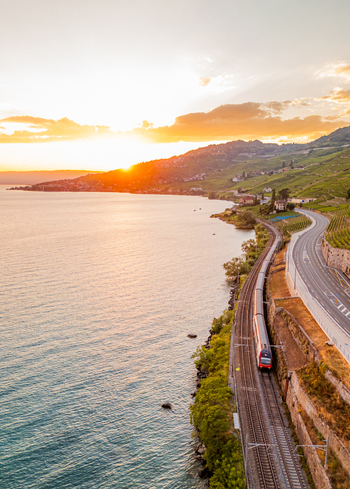 Aerial view of a train traveling along the tracks beside Lake Geneva with the terraced vineyards of Lavaux at sunset in Bourg en Lavaux Vaud Switzerland. Aerial view of a train traveling along the tracks beside Lake Geneva with the terraced vineyards of Lavaux at sunset in Bourg en Lavaux Vaud Switzerland.