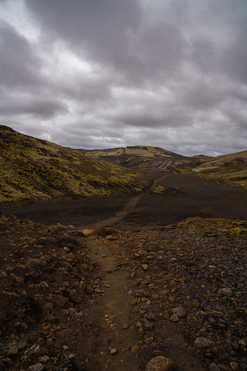 View of a rugged trail winding through black volcanic earth and moss covered hills under a brooding sky Skaftárhreppur Skaftárhreppur Iceland. View of a rugged trail winding through black volcanic earth and moss covered hills under a brooding sky Skaftárhreppur Skaftárhreppur Iceland.
