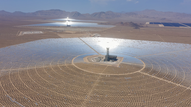 Aerial view of a large concentrated solar power plant with thousands of heliostat mirrors surrounding a central tower in a vast desert landscape United States.