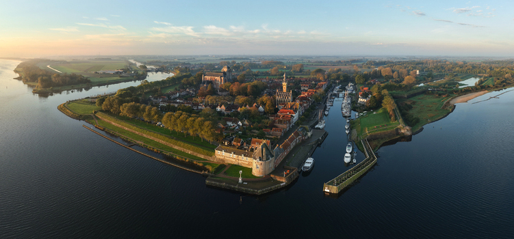 Aerial view of the historic town featuring the Grote Kerk harbor with moored boats and lush green embankments under a soft golden light Veere Zeeland Netherlands.