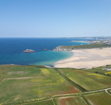 Aerial view of Polly Joke beach with its sandy cove and turquoise water surrounded by green fields and rocky headlands in Newquay Cornwall United Kingdom.