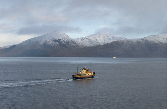 Aerial view of a vintage boat cruising on calm waters with snow capped mountains in the background Scotland United Kingdom.