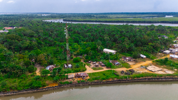 Aerial view of a telecommunications tower surrounded by small houses and lush tropical vegetation near a river in Minima Rivers Nigeria.
