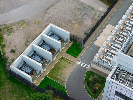 Aerial view of a data center facility with industrial generators in fenced enclosures and HVAC units on rooftops in the United Kingdom.