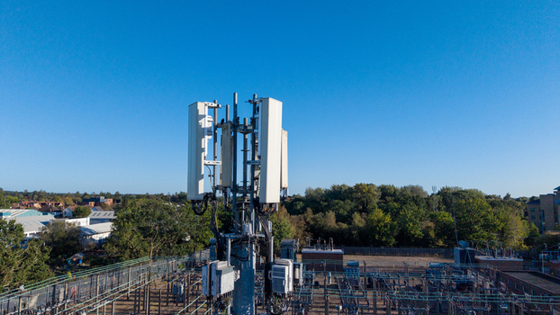 Aerial view of a telecommunications phone mast with antennas and equipment set against a clear blue sky above a power substation in Camberley England United Kingdom. Aerial view of a telecommunications phone mast with antennas and equipment set against a clear blue sky above a power substation in Camberley England United Kingdom.