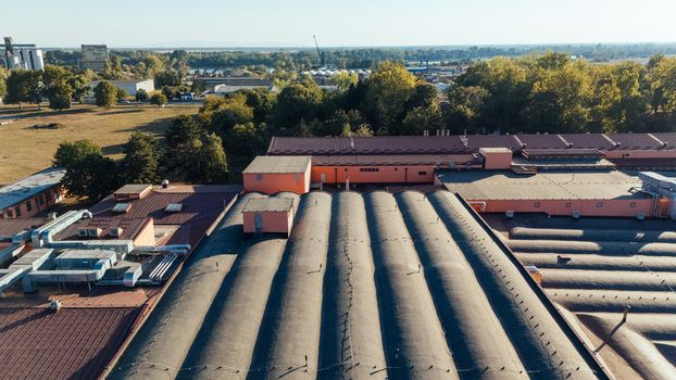 Aerial view of an industrial factory complex with large corrugated roofs and ventilation systems surrounded by green trees and open fields in Sremska Mitrovica Vojvodina Serbia. Aerial view of an industrial factory complex with large corrugated roofs and ventilation systems surrounded by green trees and open fields in Sremska Mitrovica Vojvodina Serbia.