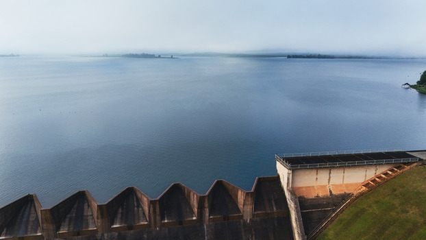 Aerial view of a concrete dam spillway and calm reservoir water under a misty morning sky in Mooi River KwaZulu Natal South Africa. Aerial view of a concrete dam spillway and calm reservoir water under a misty morning sky in Mooi River KwaZulu Natal South Africa.