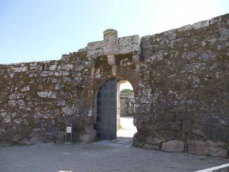View of the historic stone archway entrance at Castelo do Castro with weathered mossy walls and a metal gate in Vigo Pontevedra Spain.
